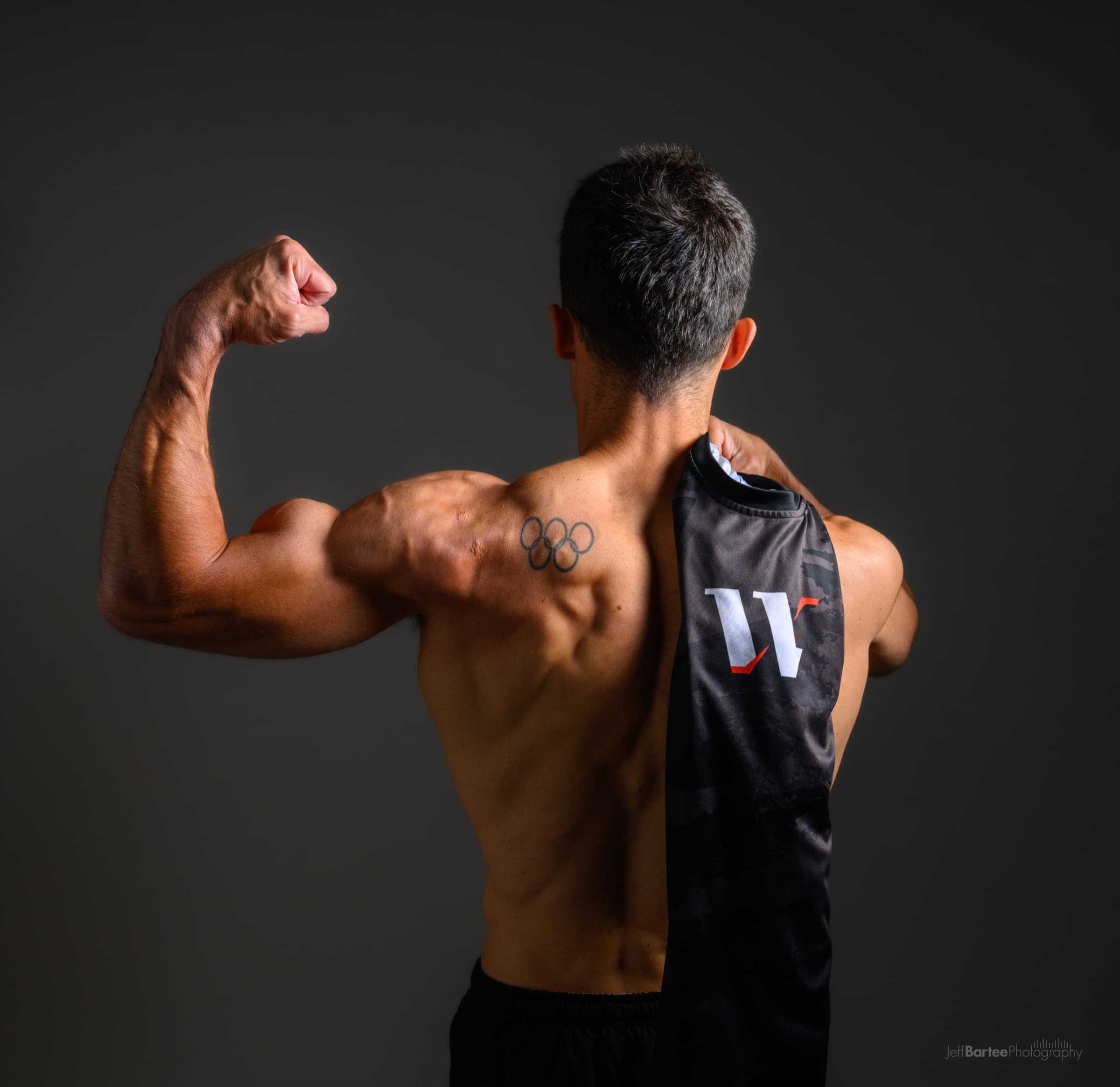 Rubén López marcando bíceps, con su tatuaje de los anillos olímpicos visible, sosteniendo una camiseta de WarmApp
